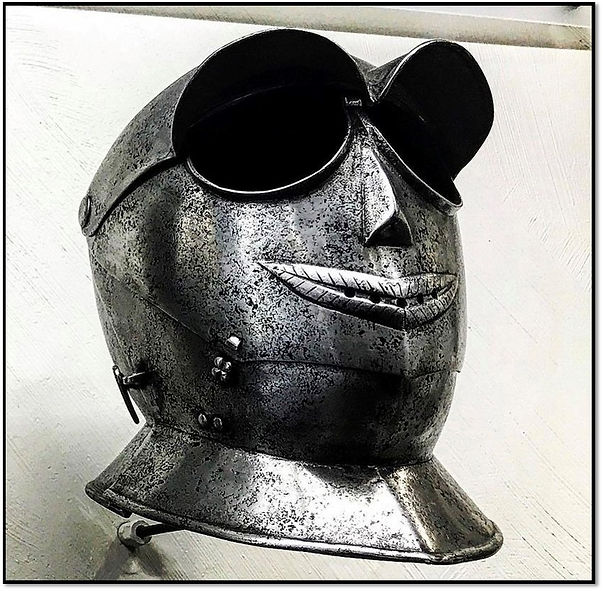Metal helmet mask sculpture with round eye openings and carved mouth, gray and black tones, eerie mood