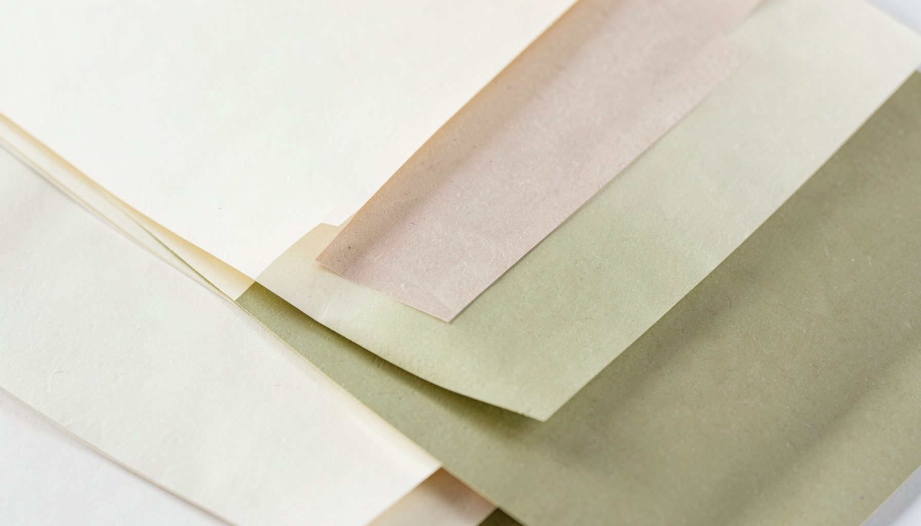Abstract composition of layered paper sheets in cream, beige, and soft olive tones, suggesting pages of a literary journal in gentle light.
