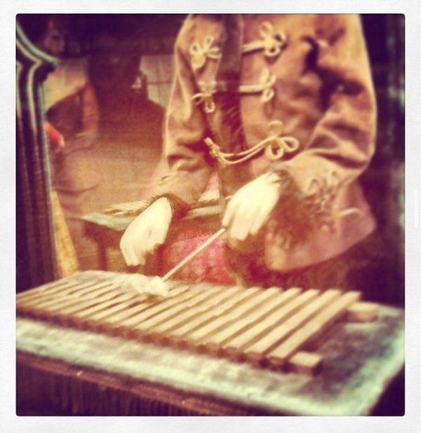 Close-up of gloved hands playing a wooden xylophone-like instrument, warm sepia tones, nostalgic mood